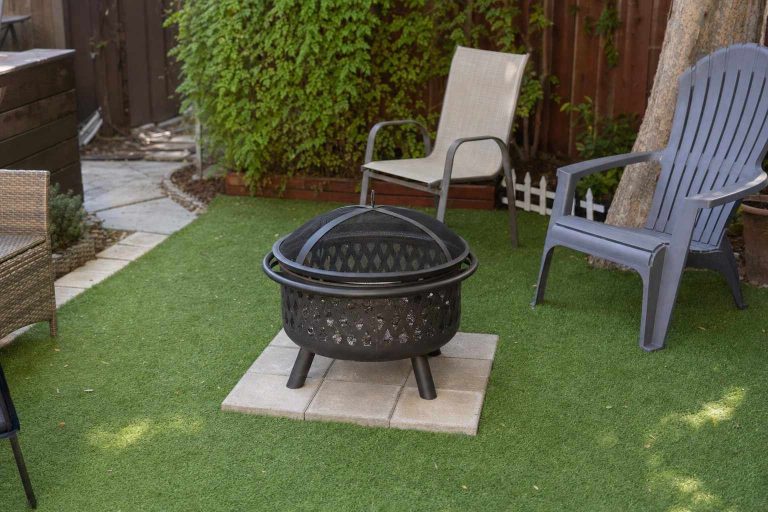 A metal fire pit on a protective paver base over green artificial grass