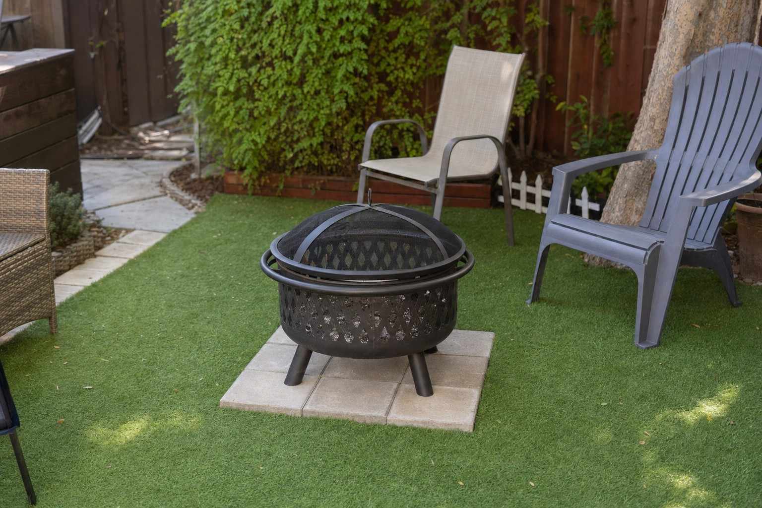 A metal fire pit on a protective paver base over green artificial grass