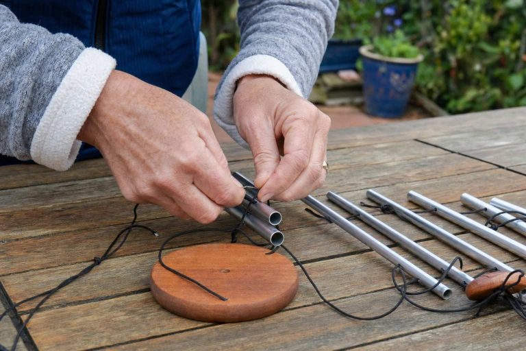 Hands restringing a metal tube wind chime with new cord on a workbench