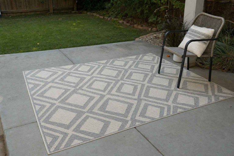 A neutral geometric outdoor rug laid on a plain grey concrete patio