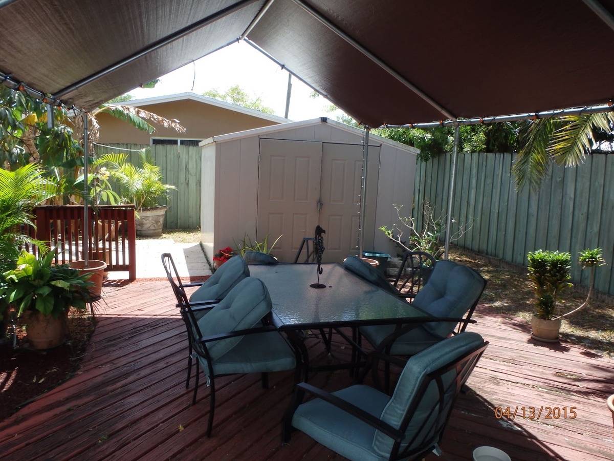 Fabric canopy shading a wooden deck with a glass-top dining set and potted palms