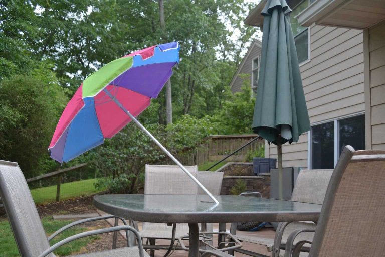 A lightweight beach umbrella propped beside a patio dining table, clearly too thin for the table hole