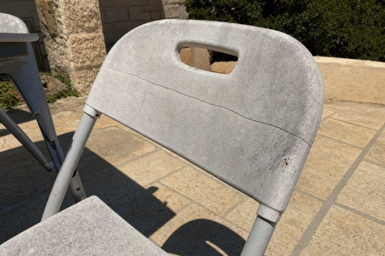 A faded and cracked plastic folding chair in harsh direct sunlight