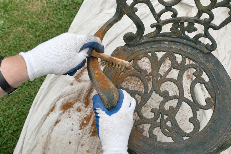 Gloved hands wire-brushing rust from an ornate cast iron garden chair