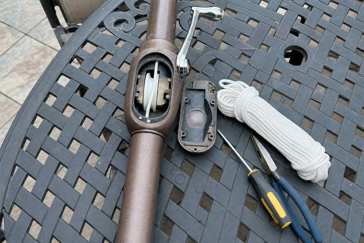 An opened patio umbrella pole on a work table with new cord and tools laid out