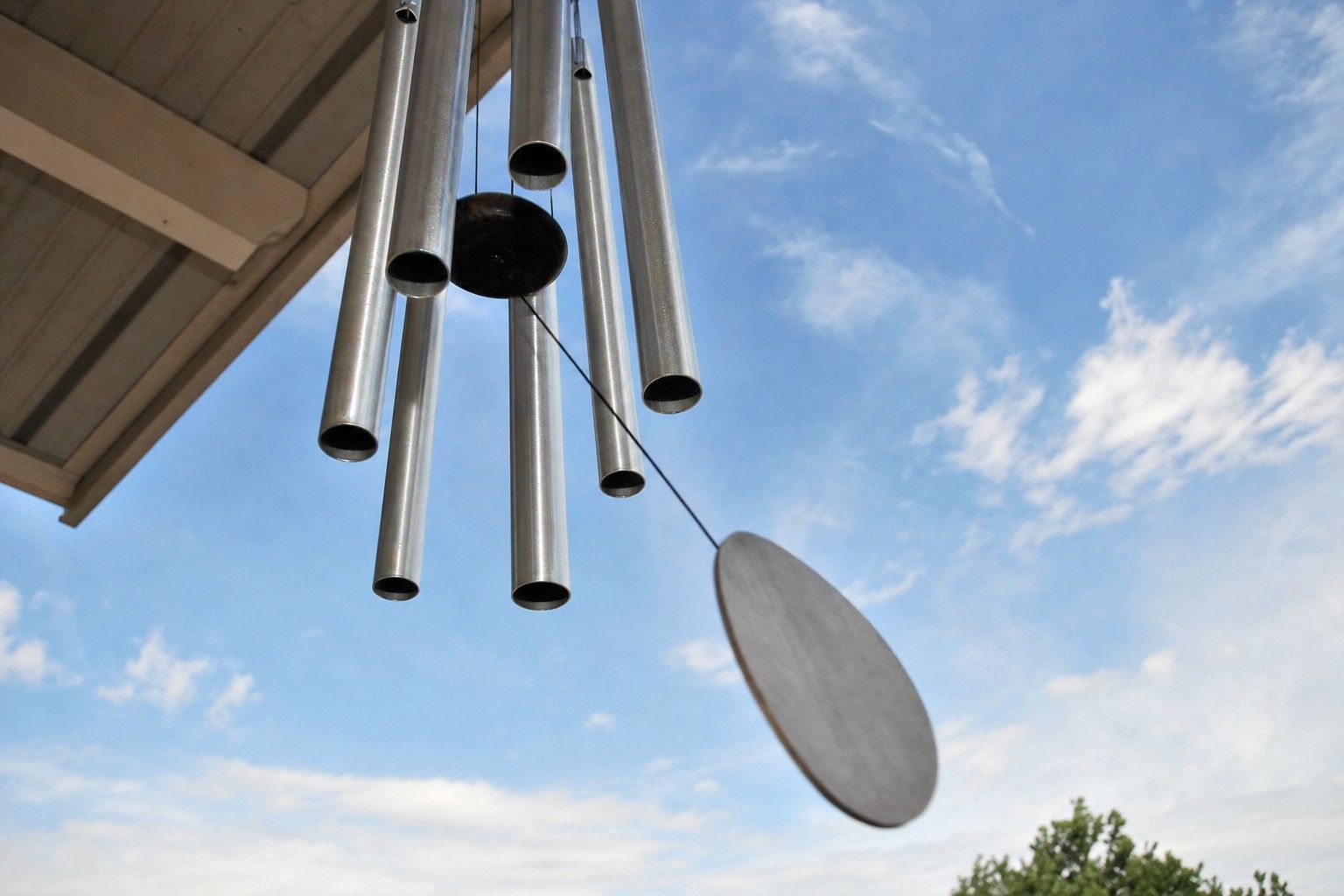 Close view of metal wind chime tubes and striker against the sky